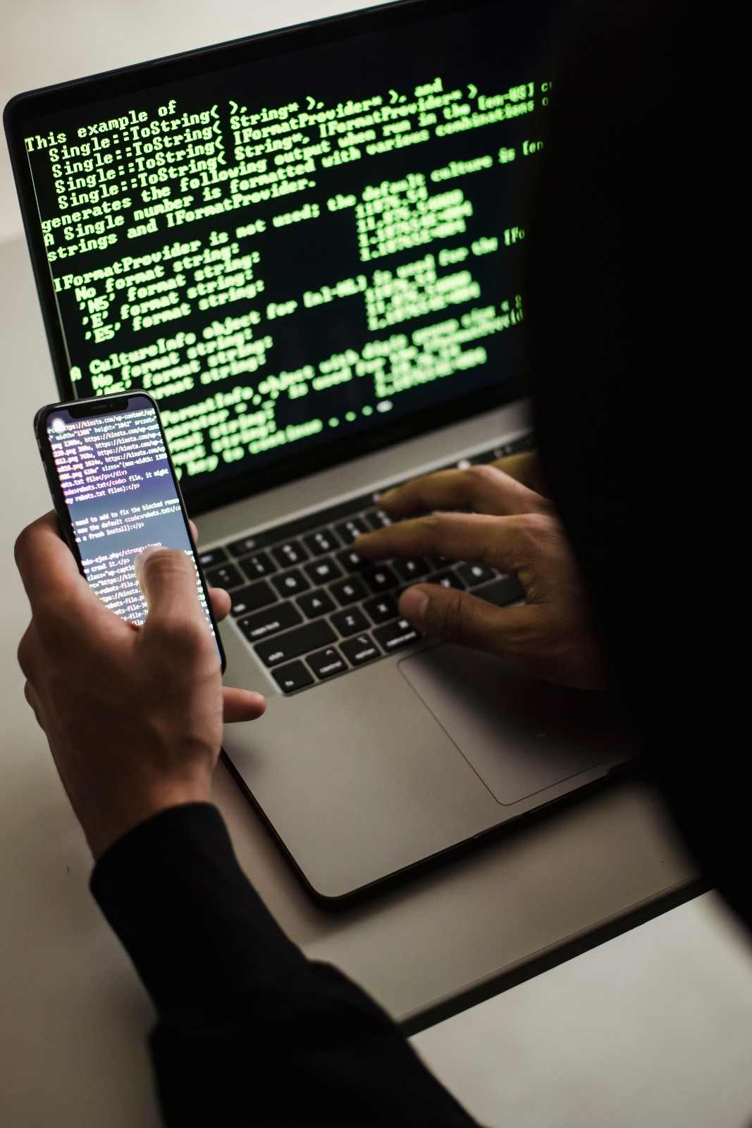 A hacker with a cellphone looking at a computer